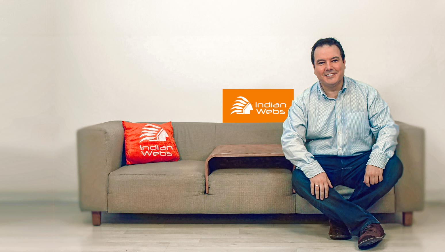 Un hombre sonriente sentado en un sofá con el logotipo de su empresa superpuesto.